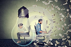 Woman sitting inside electric lamp working on computer next to entrepreneur under money rain