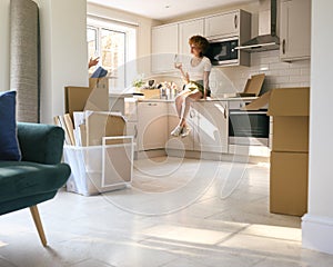 Woman Sitting On Kitchen Counter Celebrating With Wine On Moving Day In New Home