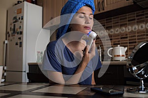 A woman is sitting in the kitchen and doing a beauty procedure using a beauty gadget