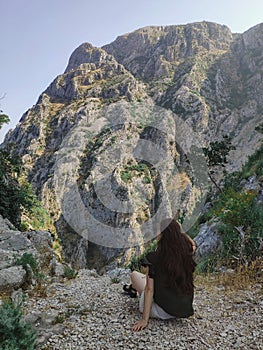 Woman is sitting and looking at mountains from above in Kotor, Montenegro