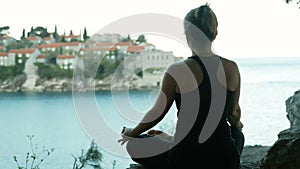 Woman sitting in lotus pose on the background of the city and the sea.
