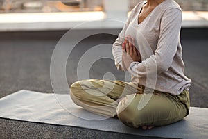 Woman sitting in lotus pose on mat and practicing yoga, female meditating outdoors