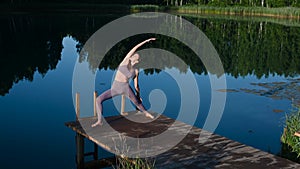 Woman sitting in lotus position and doing yoga on lake background. Beautiful girl exercising outdoors. Stretching