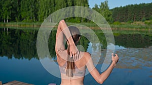 Woman sitting in lotus position and doing yoga on lake background. Beautiful girl exercising outdoors. Stretching