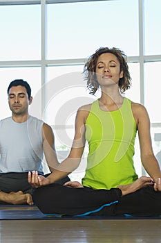 Woman Sitting In Lotus Position With Man In The Background