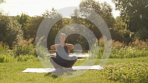 Woman sitting in lotus position on yoga mat and feeling harmony of her body and nature. Female meditating at sunrise in park. Heal