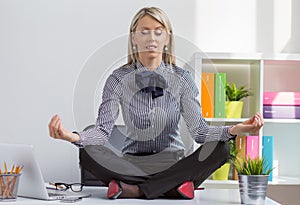 Woman sitting in lotus yoga pose on desk in office