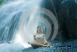 Woman sitting lotus yoga pose in spiritual relaxation serenity and meditation at stunning beautiful waterfall and rain forest in B