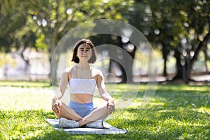 A woman is sitting on a mat in a park, looking up at the sky