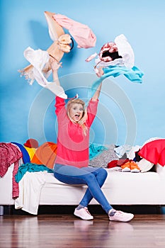 Woman sitting on messy couch throwing clothes