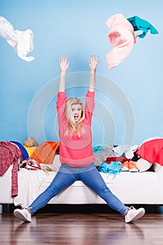 Woman sitting on messy couch throwing clothes