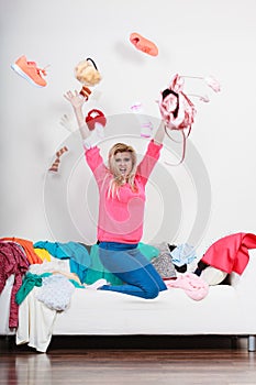 Woman sitting on messy couch throwing clothes