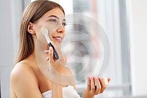 Woman sitting by the mirror and applying makeup