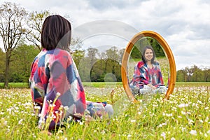 Woman sitting with mirror in blooming meadow