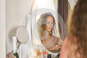 Woman sitting at mirror putting on makeup