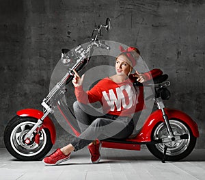 Woman sitting on motorcycle bicycle scooter retro pinup style pointing finger at the corner in red blouse and jeans