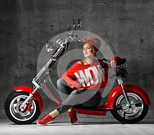 Woman sitting on motorcycle bicycle scooter retro pinup style in red blouse and jeans