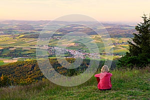 A woman sitting on mount Hohenbogen, looking to Neukirchen Heiligblut, a small town in the Bavarian Forest