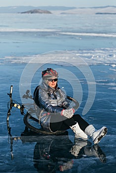 Woman sitting near her bike on ice. The girl cyclist stopped to rest. She sits on the wheel and enjoys the beautiful