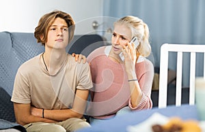 Woman sitting near her sad son and calling to doctor