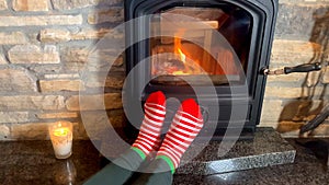 Woman sitting near a hot burning fireplace, legs stretched out in red socks to the fire, concept of winter relaxation