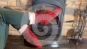 Woman sitting near a hot burning fireplace, legs stretched out in red socks to the fire, concept of winter relaxation