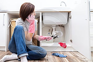 Woman sitting near leaking sink sking for help by phone