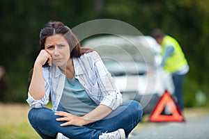 woman sitting near warning triangle and broken car on road