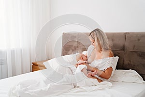 woman is sitting with a newborn in a white bed feeding breast milk.