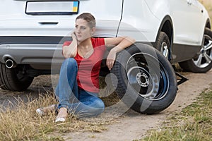 Woman sitting next to the car with flat tire and waiting for help