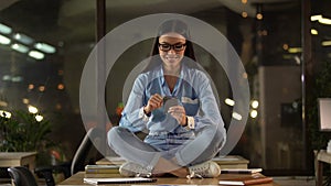 Woman sitting on office desk, using cell phone, excited with mobile application