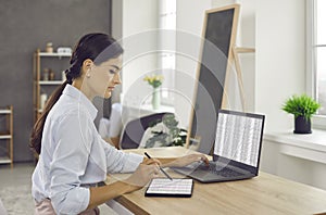 Woman sitting at office desk, working on laptop and tablet computers and using stylus pen