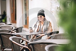 Woman sitting on open terrace of street cafe, using her samrtpho