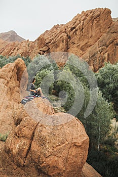 Woman sitting on oriental carpet on background of Todra gorge canyon in Morocco