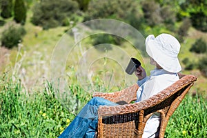 Woman sitting outside on a wicker bench with cup