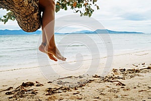 Woman sitting on palm tree at tropical beach