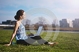 Woman sitting in park on the green grass with laptop. Computer screen mockup. Student studying outdoors. Copy space for text. Beau