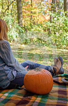 Woman sitting on picnic blanket with pumpkin in autumn