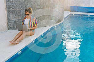 Woman sitting by the pool typing on her laptop
