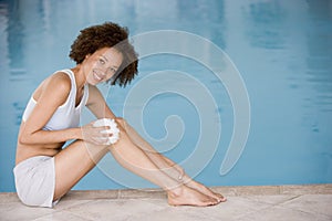 Woman sitting poolside using shower puff