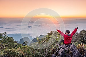 Woman sitting and raise hands up on hill with fog in sunrise at wildlife sanctuary