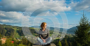 A woman sitting, resting high in the mountains. on a sunny day, spring, blue sky and white clouds on the background and a little t