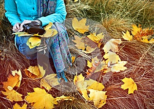 Woman sitting with retro camera and autumn leaves