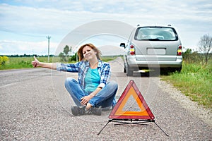 Woman sitting on road near emergency sign showing thumbs up