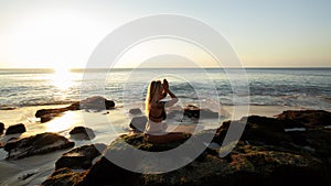 Woman sitting on the rock, practicing yoga and enjoying ocean view. Hands in namaste mudra. Yoga on the beach, Bali