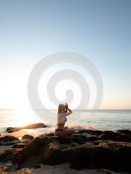 Woman sitting on the rock, practicing yoga and enjoying ocean view. Hands in namaste mudra. Yoga on the beach, Bali