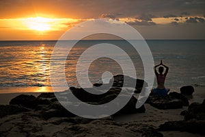 Woman sitting on the rock, practicing yoga and enjoying ocean view. View from back. Hands in namaste mudra. Yoga at the beach