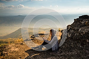 A woman sitting on rocky mountain using smartphone and looking out at beautiful natural view