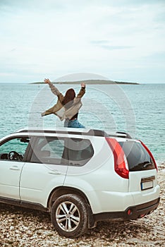 Woman sitting on the roof of the car enjoying view of sea