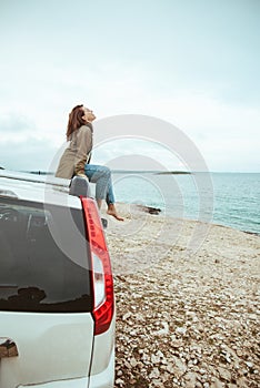 woman sitting on the roof of the car enjoying view of sea